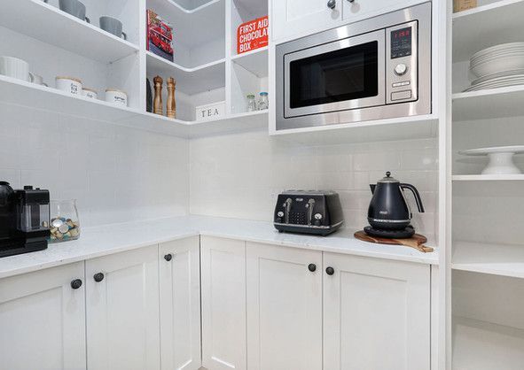 A kitchen with white cabinets , a microwave, a toaster and a kettle.