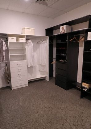 A walk in closet with white shelves and black drawers.
