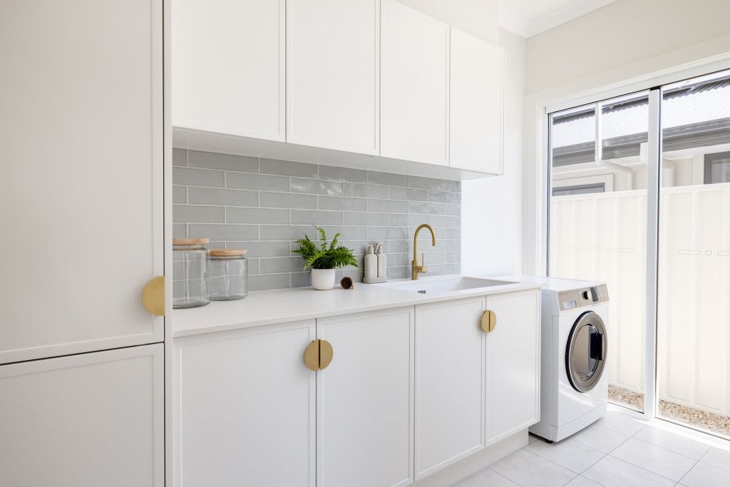 A laundry room with a washing machine, sink and cabinets.