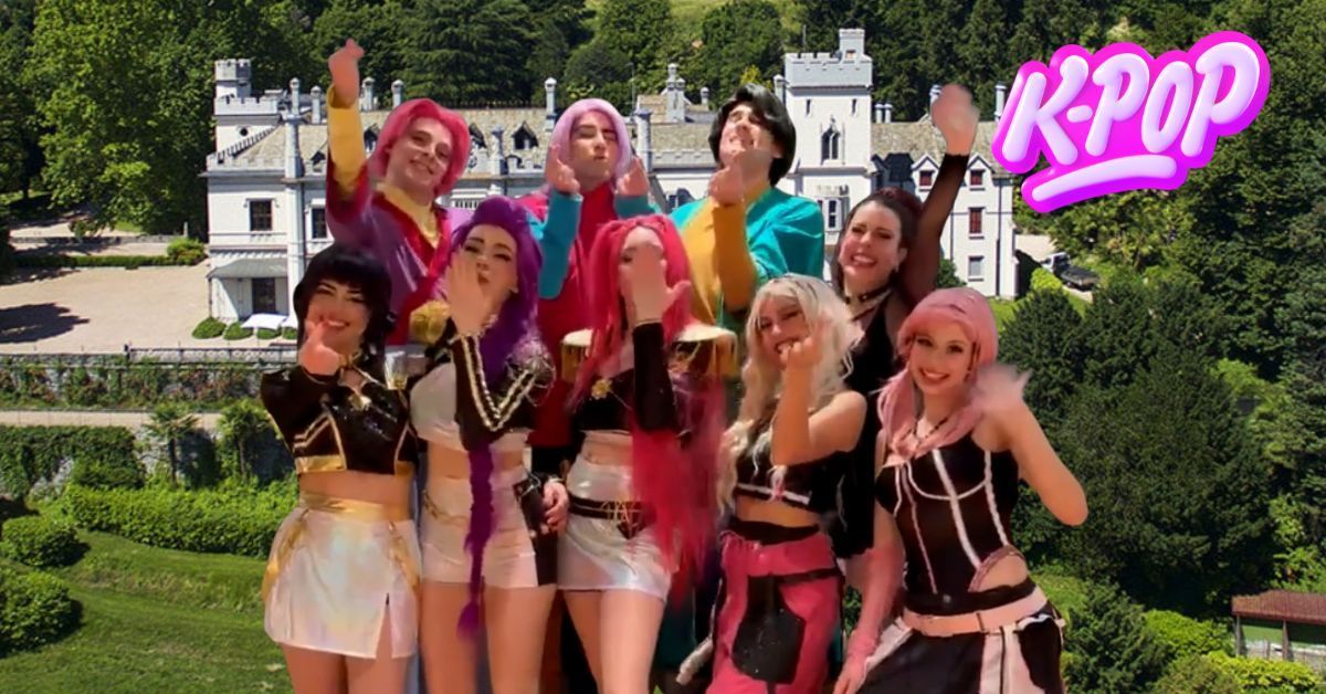 Un gruppo di ballerini vestiti con abiti colorati posa all'aperto in un giardino, con un cartello rosa con la scritta 