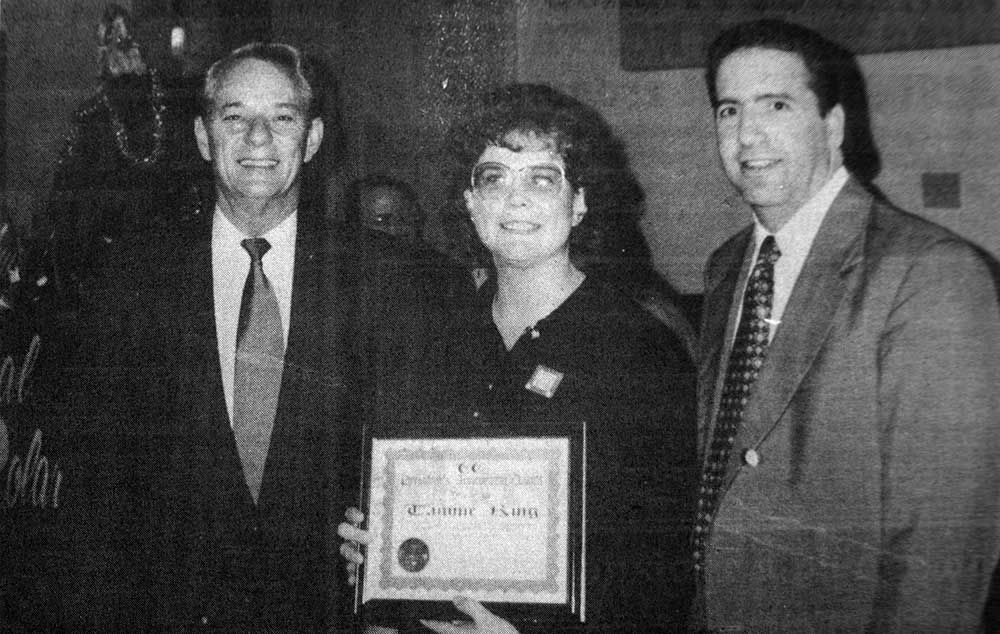 A black and white photo of two men and a woman holding a certificate