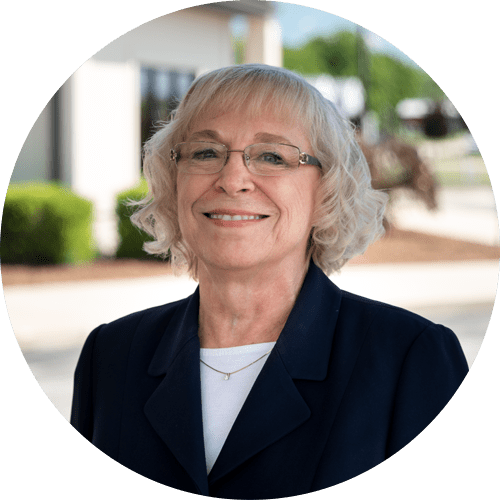 A woman wearing glasses and a blue jacket is smiling in a circle.