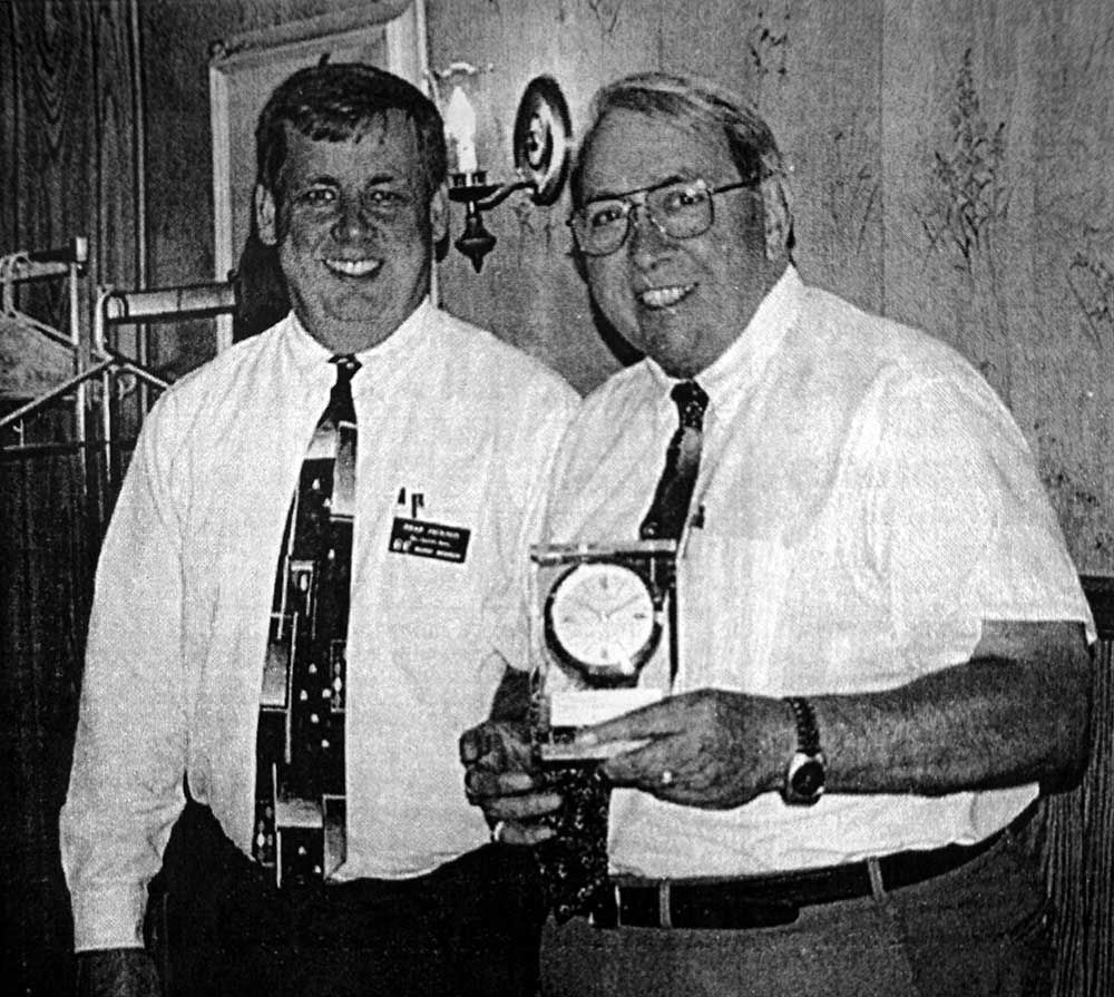 Two men standing next to each other with one holding a clock