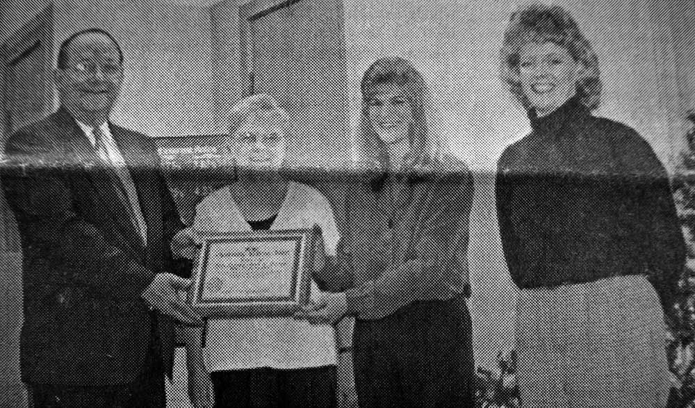 A black and white photo of a man and two women holding a certificate.