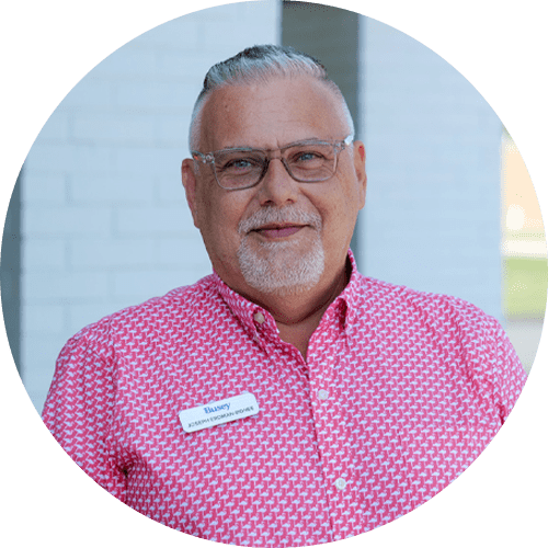 A man wearing glasses and a pink shirt is standing in a circle.