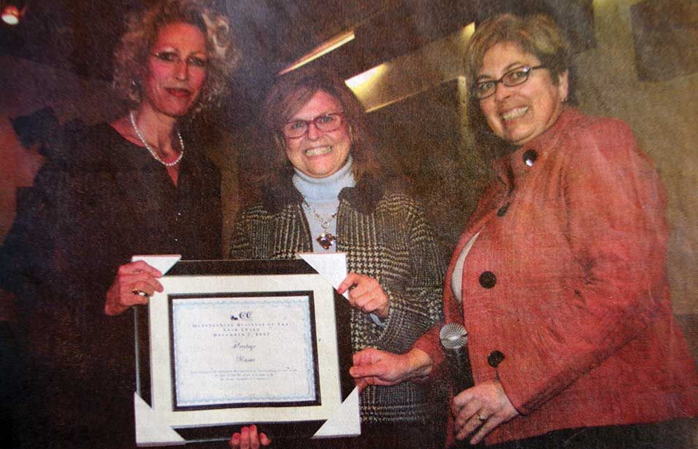 Three women are standing next to each other holding a framed certificate.