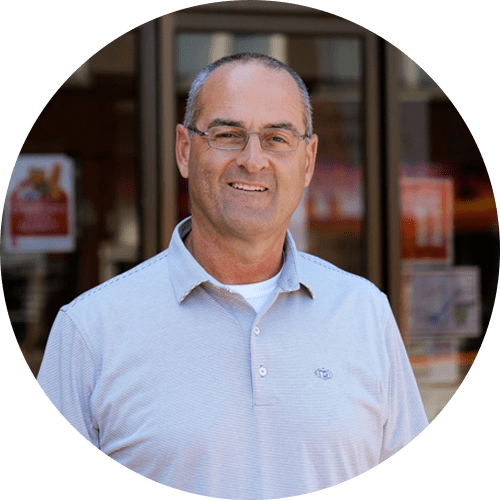 A man wearing glasses and a grey shirt is standing in front of a store.