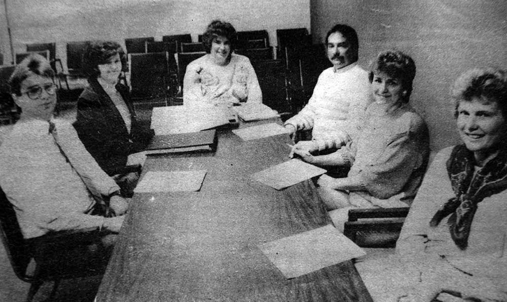 A group of people are sitting around a table in a black and white photo.