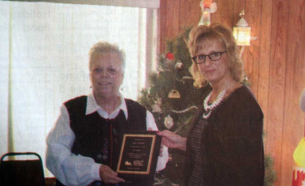 Two women are standing next to each other holding a plaque in front of a christmas tree.