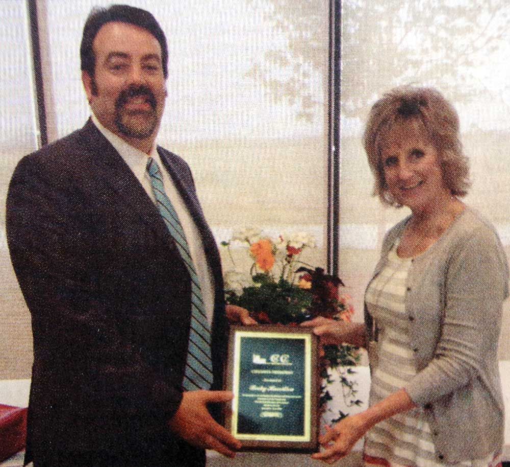 A man in a suit and tie is giving a woman a plaque