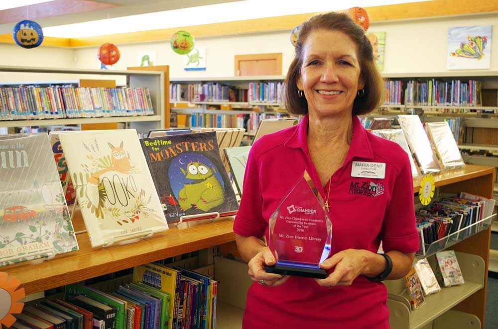 A woman in a pink shirt is holding a trophy in a library.
