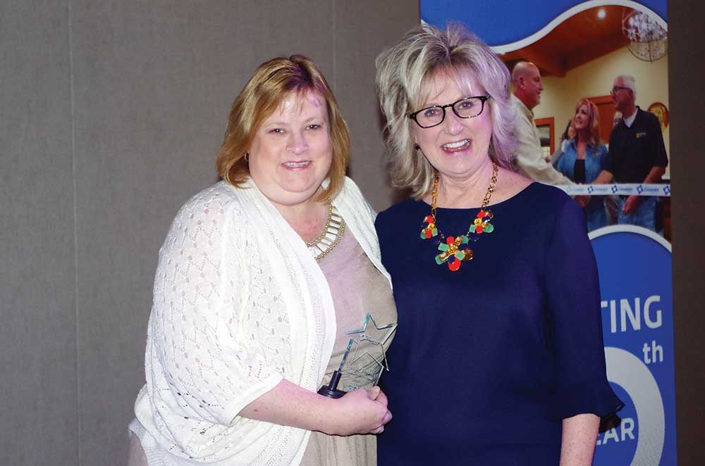 Two women are shaking hands in front of a sign that says ing