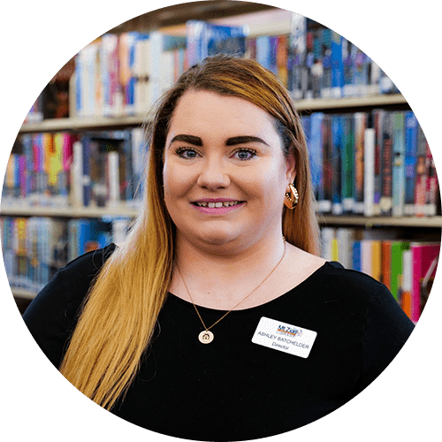 A woman is smiling in front of a bookshelf in a library.