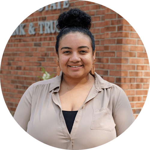 A woman is standing in front of a brick wall and smiling.
