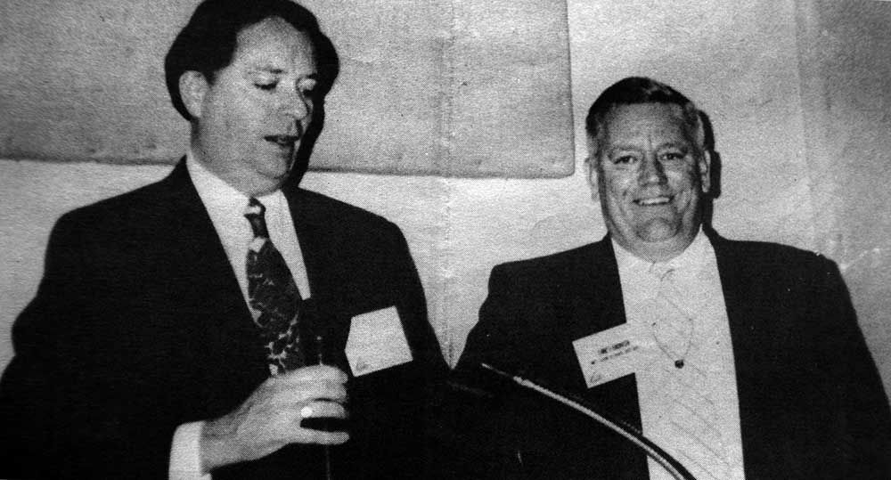 Two men in suits are standing next to each other in front of a microphone.