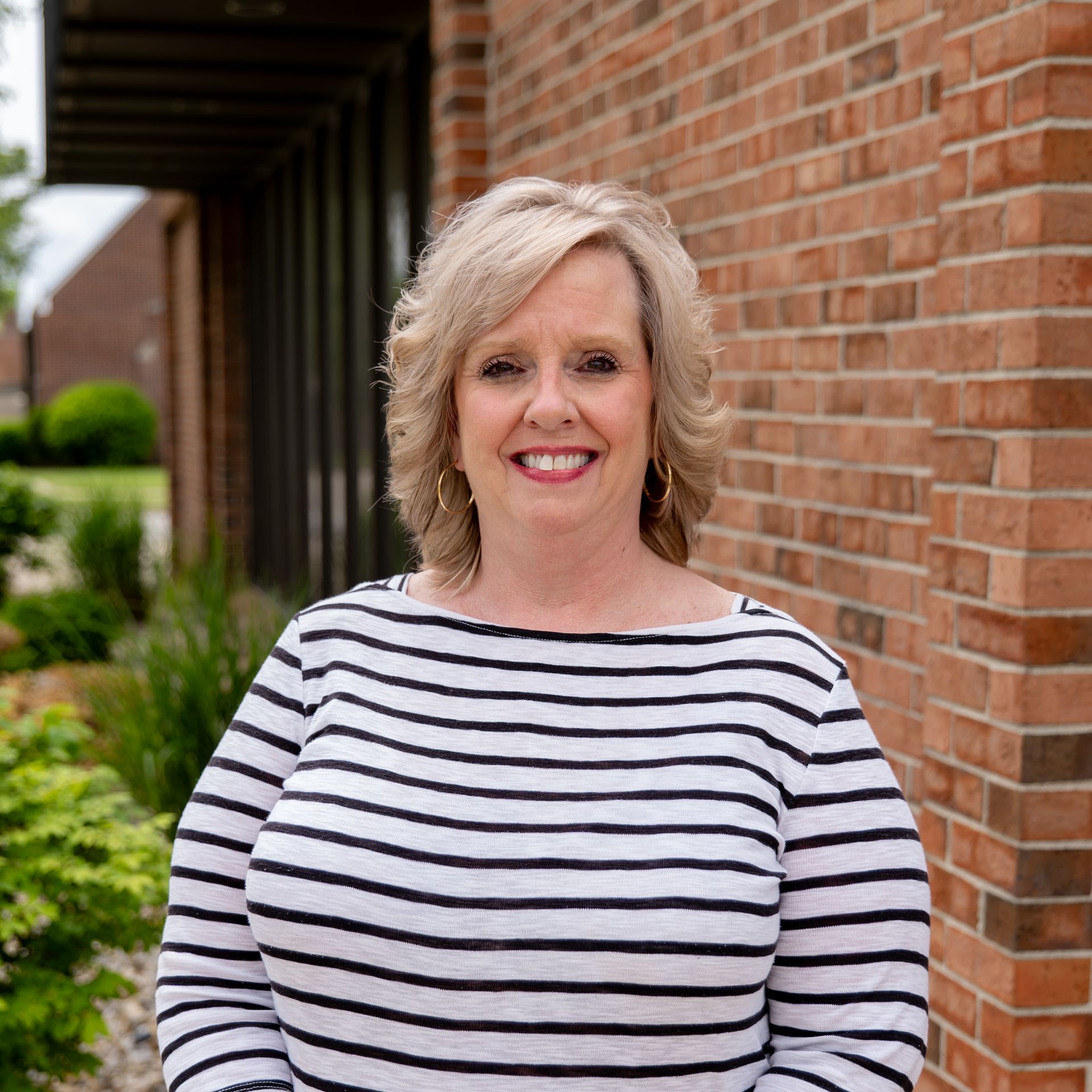 A woman in a striped shirt is smiling in front of a brick building.