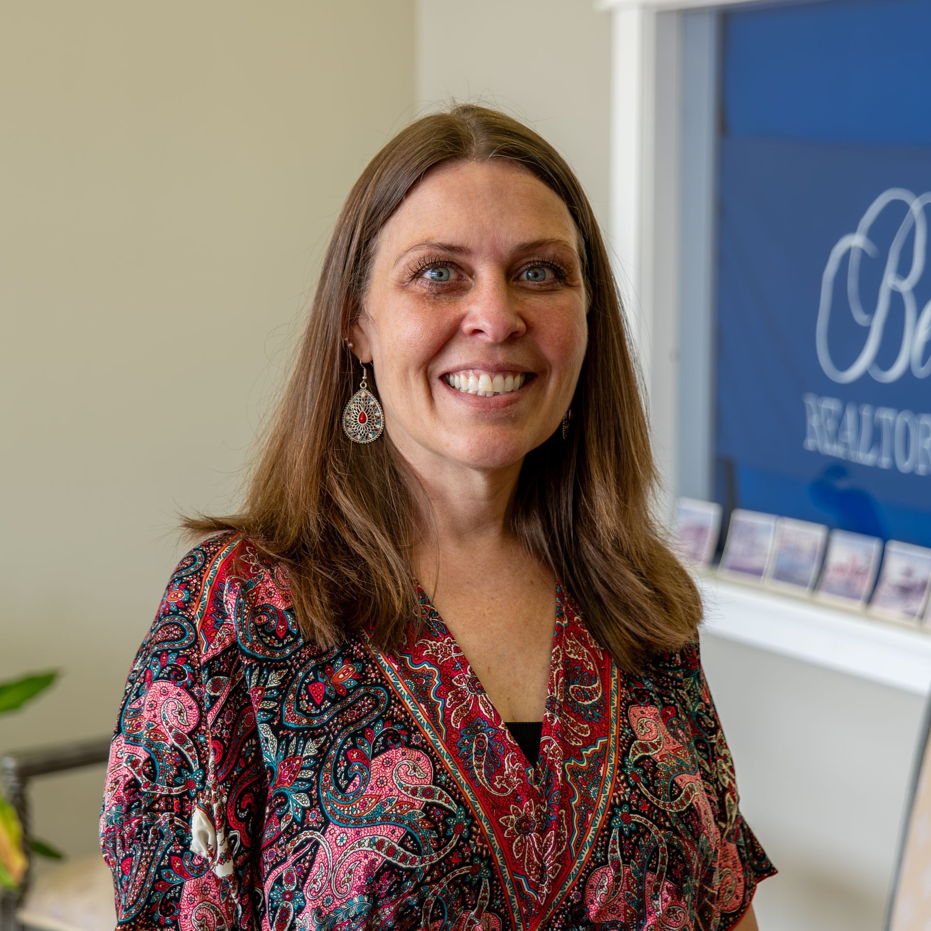A woman is smiling in front of a sign that says realtor.