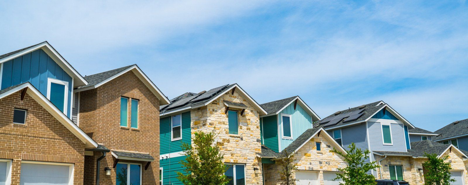 Row of colorful houses under a bright blue sky with wispy clouds.