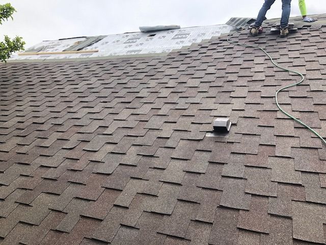 Roofer installing shingles on a brown asphalt shingle roof, partial tear-off, cloudy day.