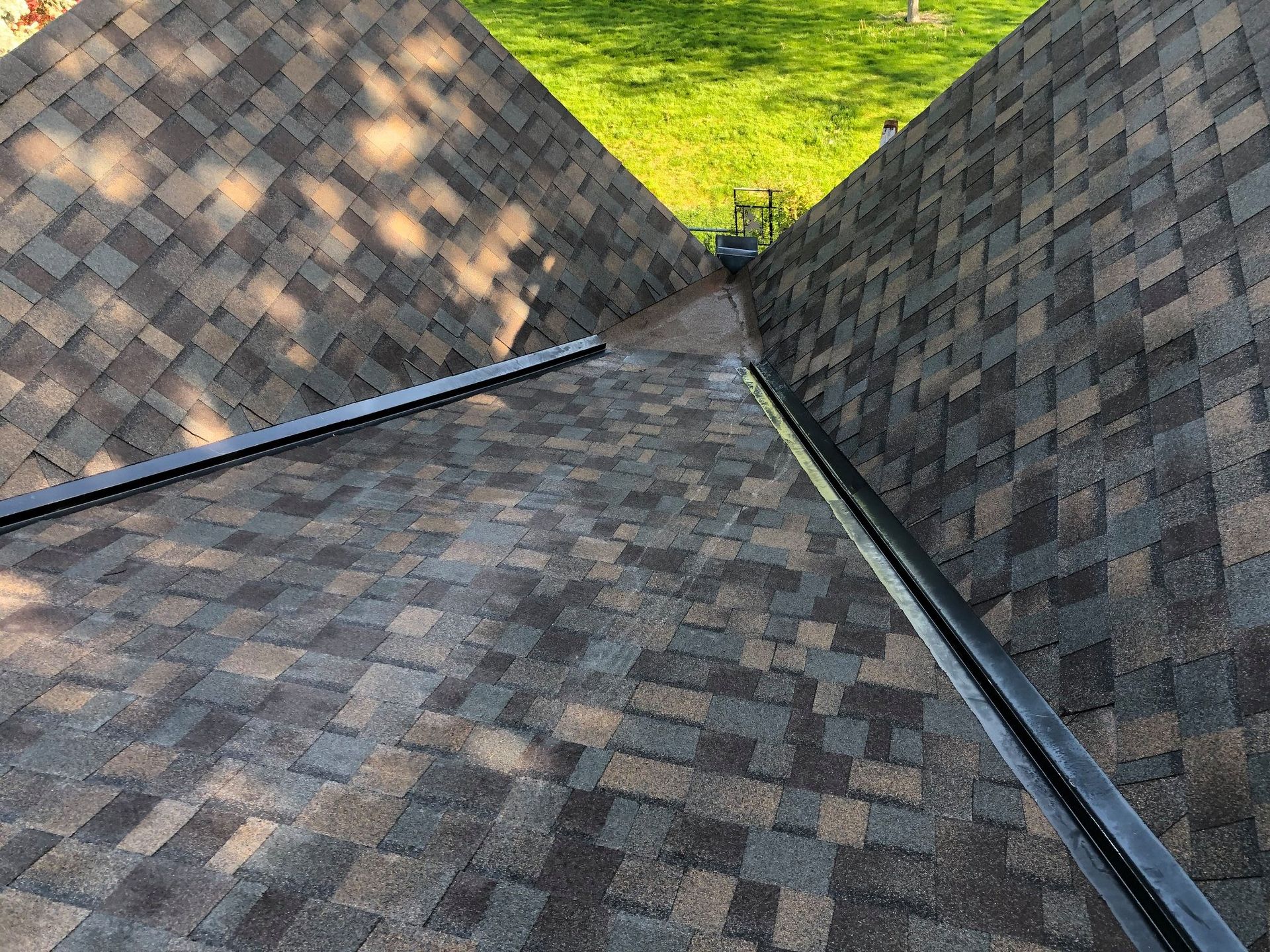 Close-up view of a brown shingle roof with a dark metal valley between two sloped sections.