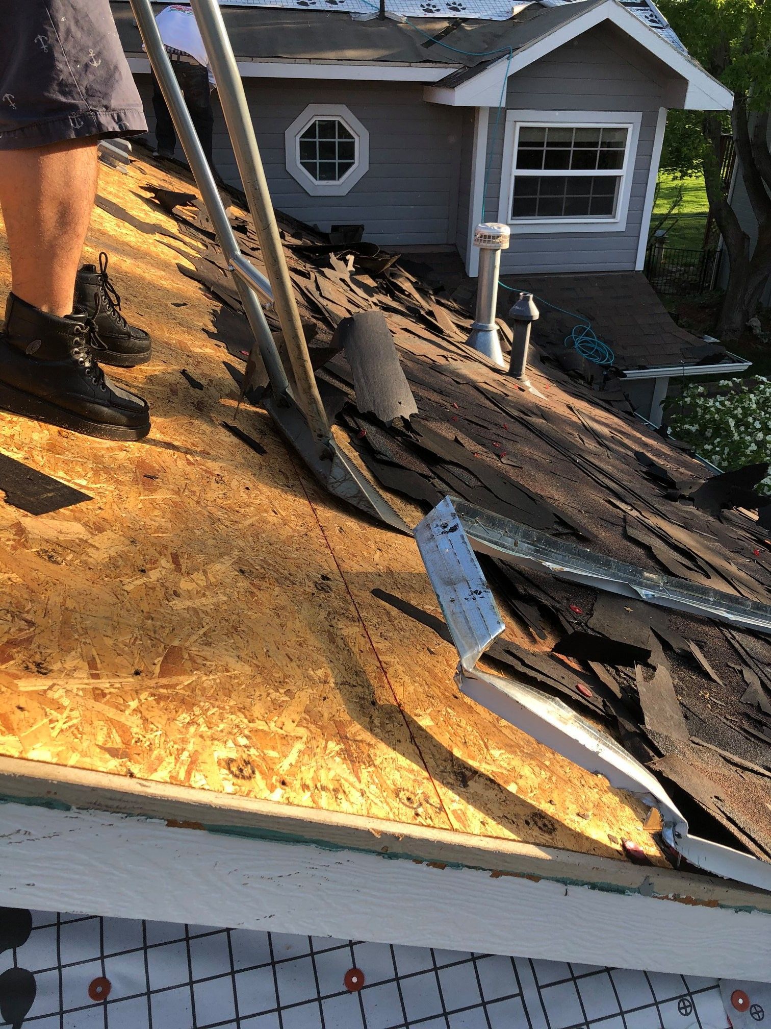Person removing roof shingles with a tool; roof of a small house.