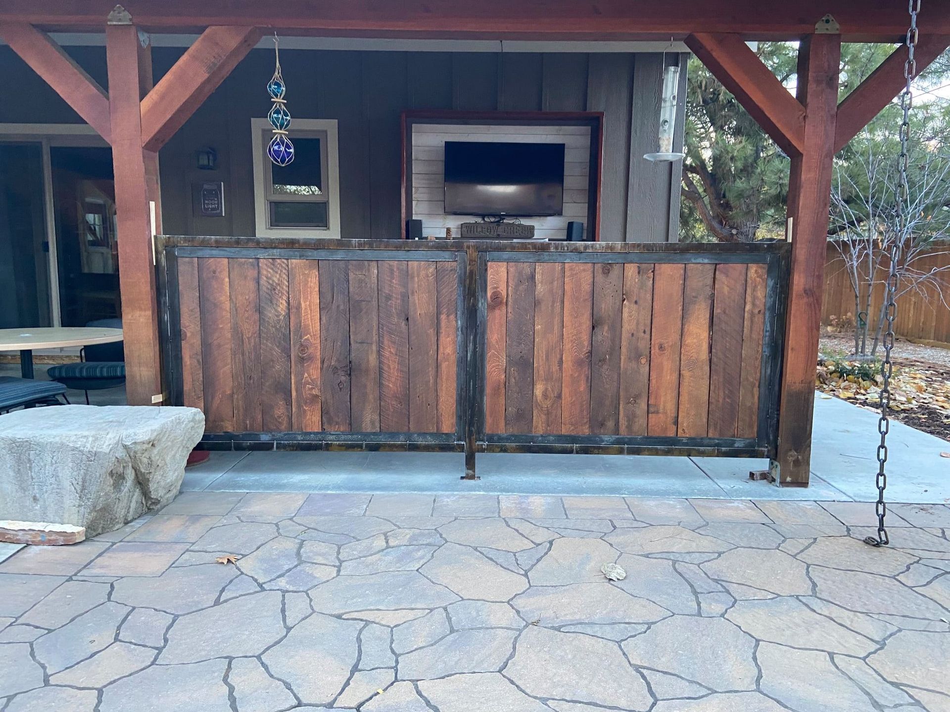 Outdoor patio with wooden bar, stone patio, and TV. Brown wood, gray stone, daytime.