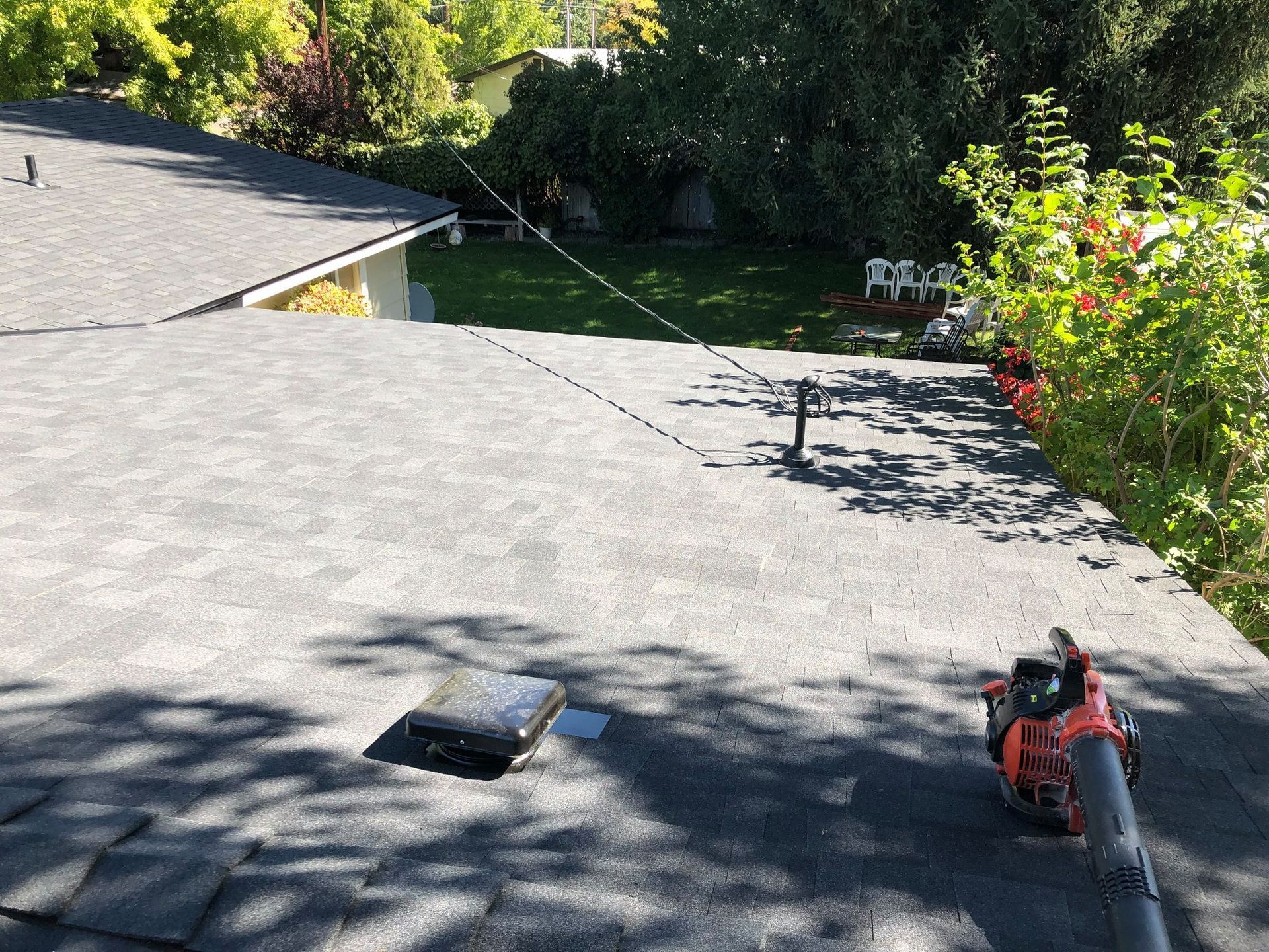 Rooftop view with a leaf blower, cable, and trees in the background.