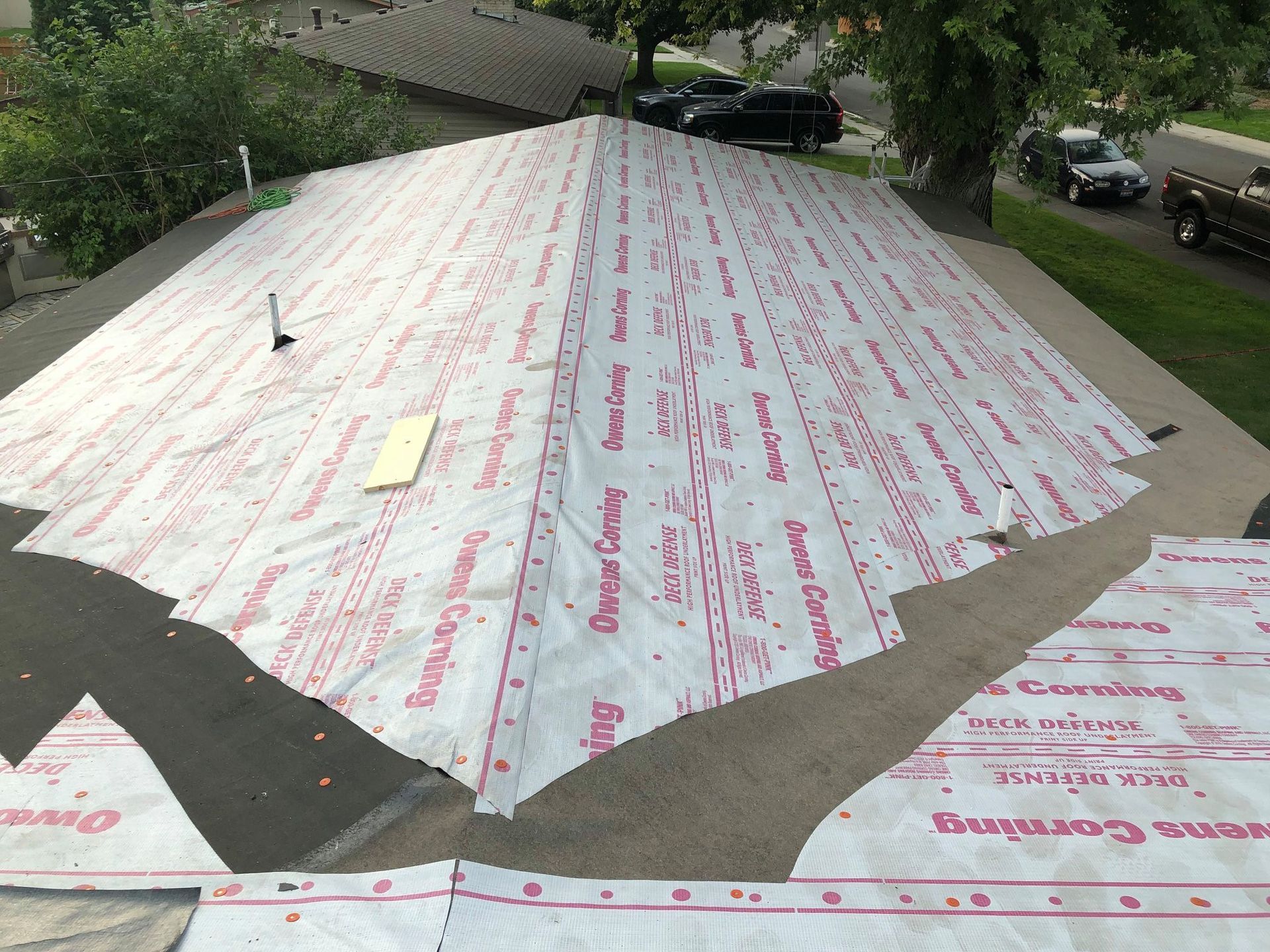 Roof with white underlayment; two-story house. Cars parked in the distance.