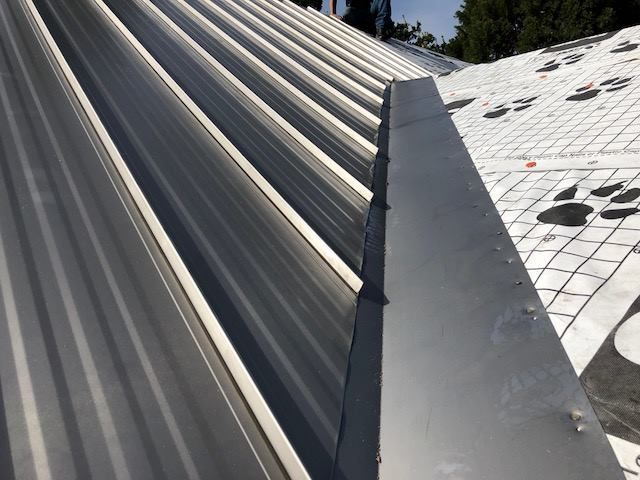 Close-up of a metal roof with vertical ridges and a gray metal flashing along the edge.