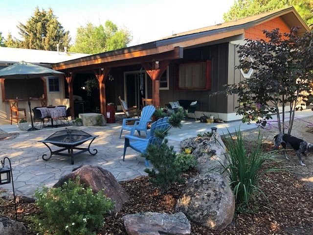 Backyard patio with blue chairs, fire pit, and landscaping; house exterior in background.