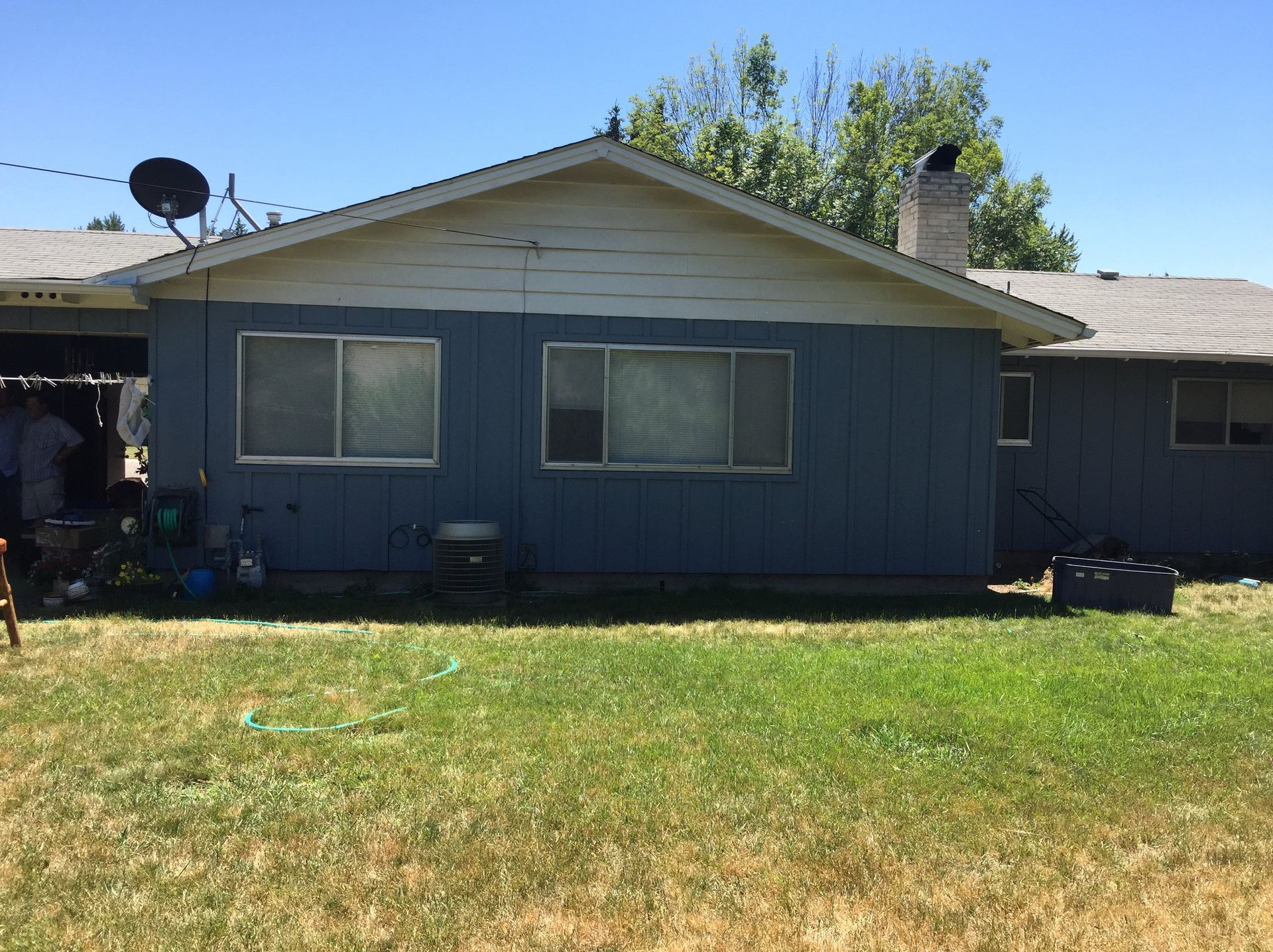 Blue house with white trim, two windows, green grass, and a satellite dish.