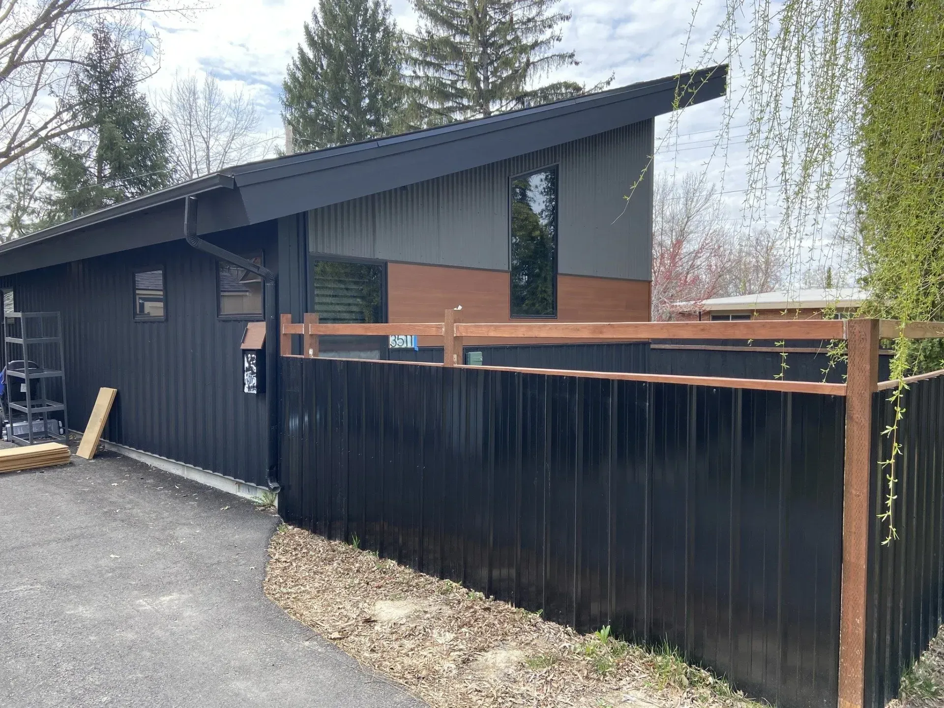 Black and gray modern house with a black fence and a driveway.