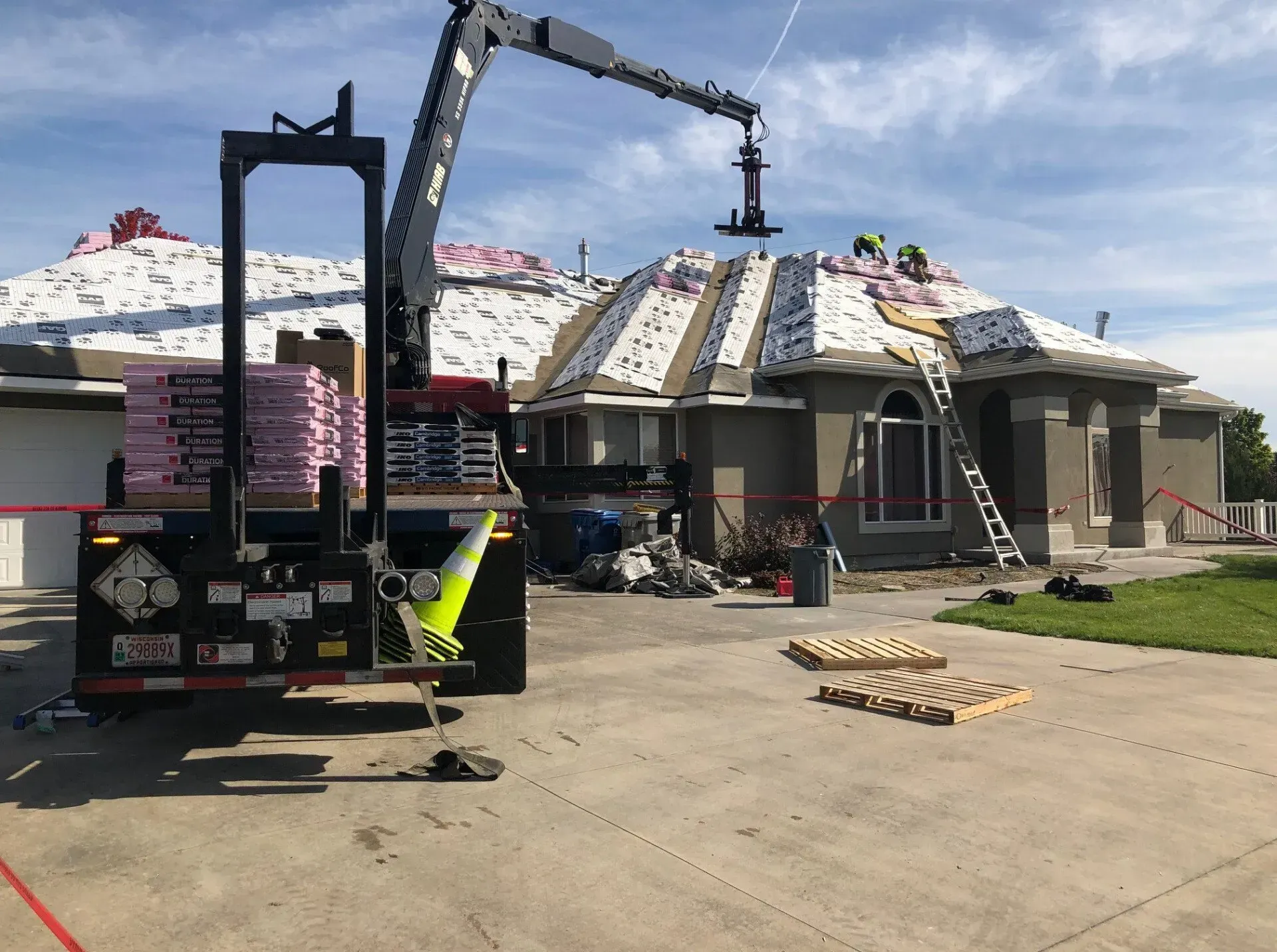 Roofers using a crane to install shingles on a house. Truck in foreground holding materials.