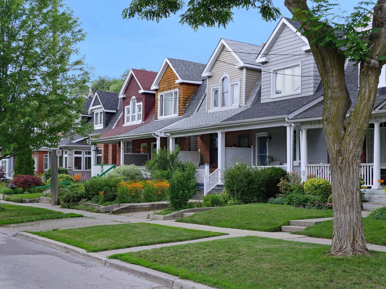 Row of colorful houses with front yards and trees on a sunny street.