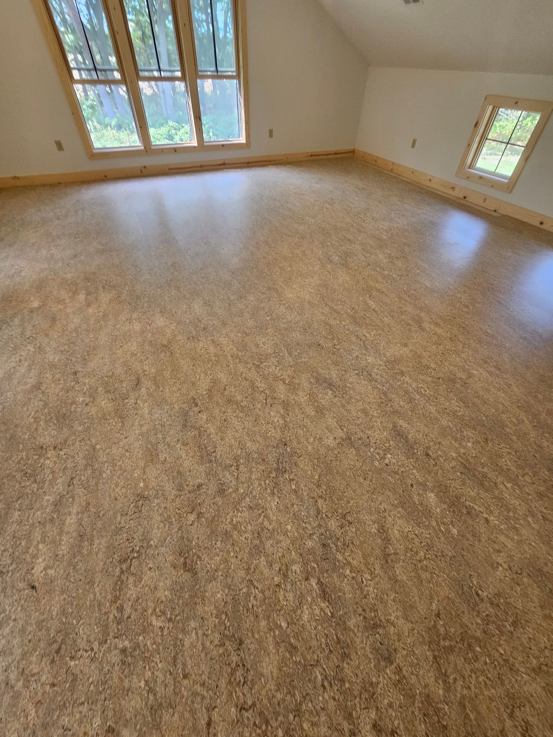 Cork flooring in an empty room with windows and wood trim.