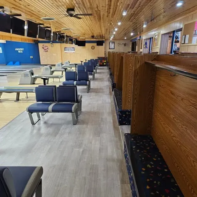 Bowling alley interior with blue seating and wooden lanes, and a wooden ceiling.