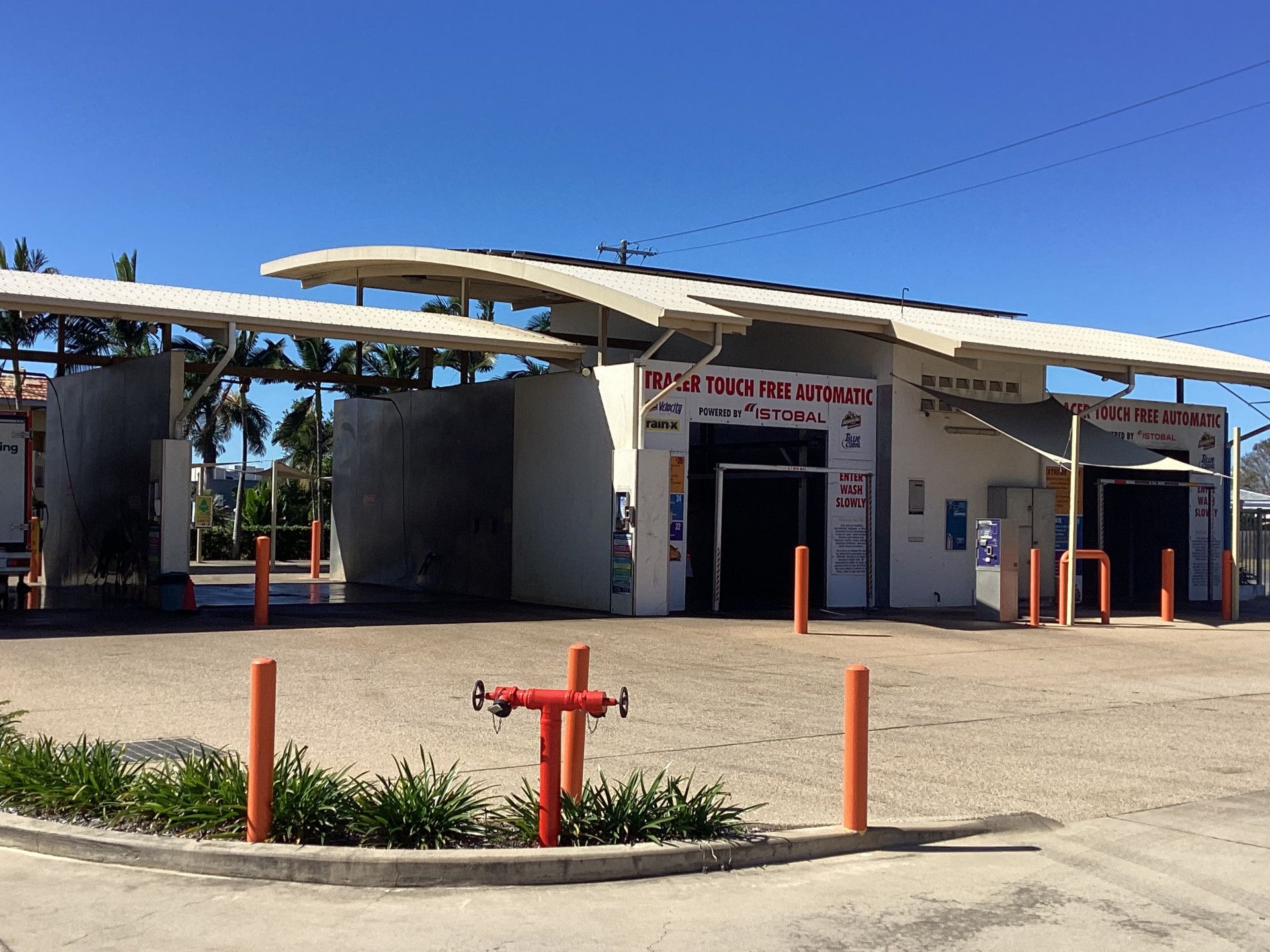 Car wash building with drive-through bays, white walls, and orange poles in front, under a bright blue sky.— Whitsunday Wash In Bowen, QLD