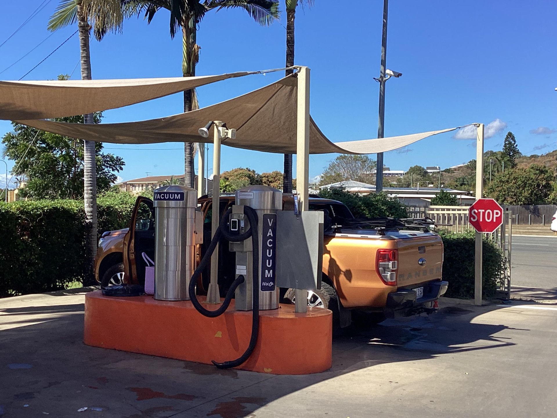 Car vacuum station with orange and tan features, under a sun shade. A pickup truck is parked at a station.— Whitsunday Wash In Bowen, QLD