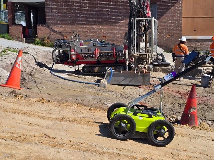 A square hole dug in grass next to a paved walkway, with a tool resting in place and a can nearby.