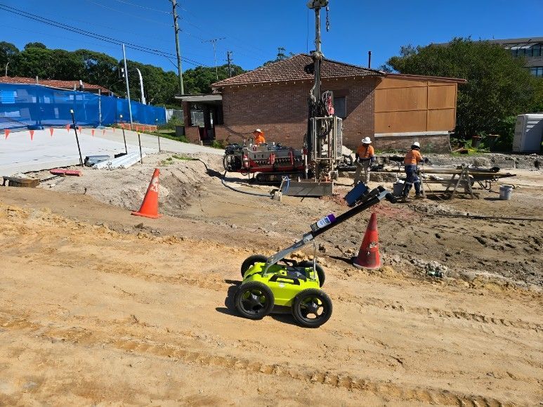 Yellow robot on construction site, drilling equipment and workers in background.