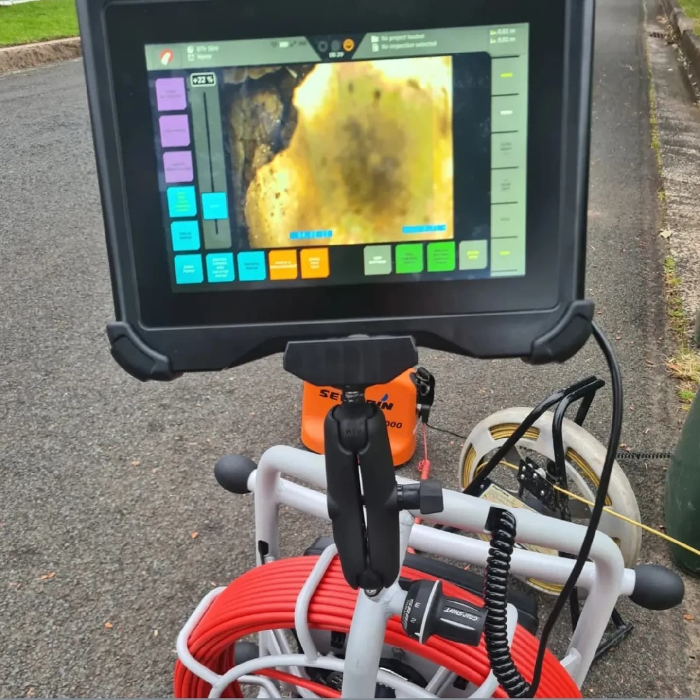 A sewer camera inspection device set up on a street, showing a close-up of a pipe interior on the screen.