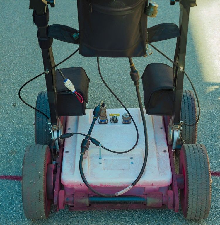 Close-up view of a pink and white mobile cart with four wheels and a black seat and armrests.