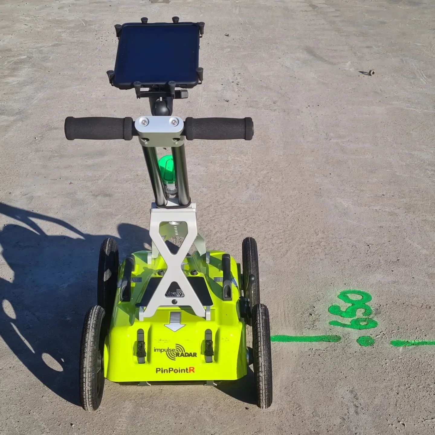 Person using an orange and black tool on the ground, wearing an orange safety vest, and black work boots.