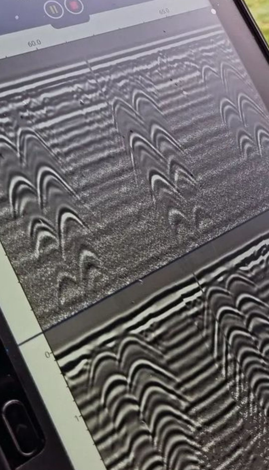 A close-up of a screen displaying a gray and white Ground Penetrating Radar (GPR) scan with arched patterns.