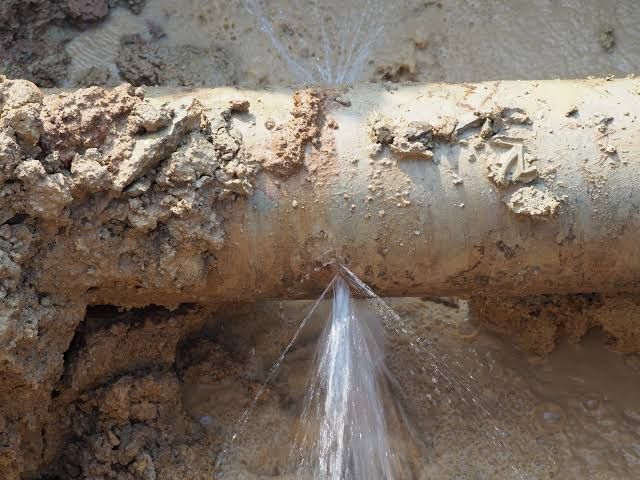 Water gushing from a damaged, buried pipe in dirt.
