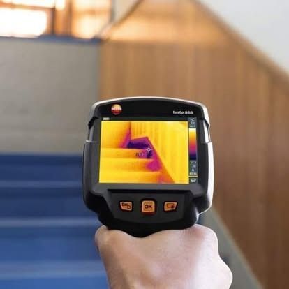 Hand holding thermal imaging camera, displaying a colorful image of a staircase, with orange and yellow hues.