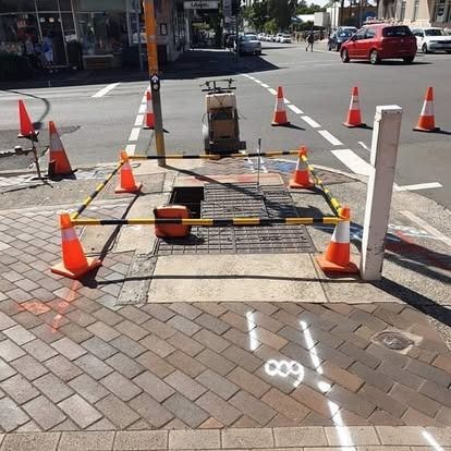 Parking lot with orange traffic cones, curb, and sunlit background of hills and sky.