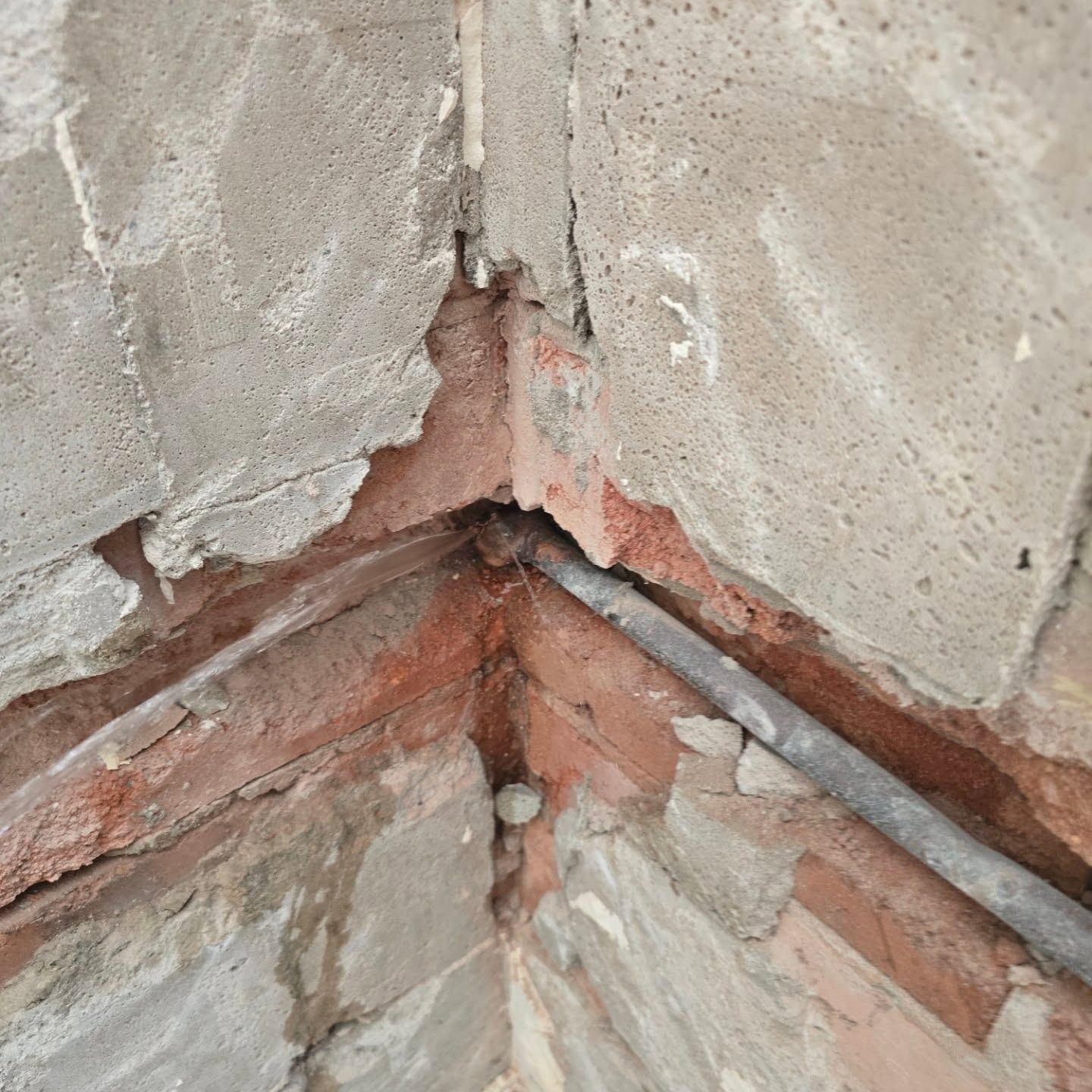 Corner of a brick wall with exposed conduit and damaged concrete.