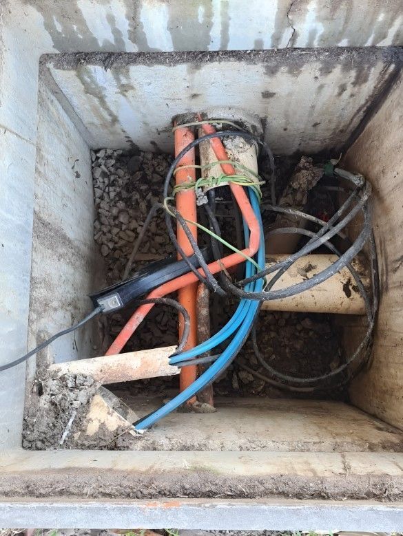 Concrete utility box with orange, blue, and black cables, gravel and a wood block inside.