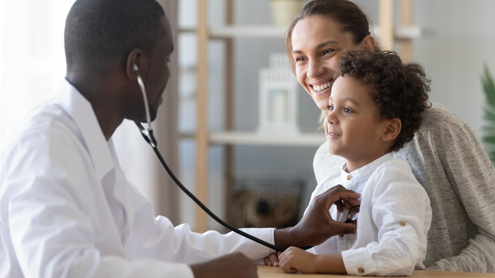 Doctor examining a child while a smiling parent watches in a clinic